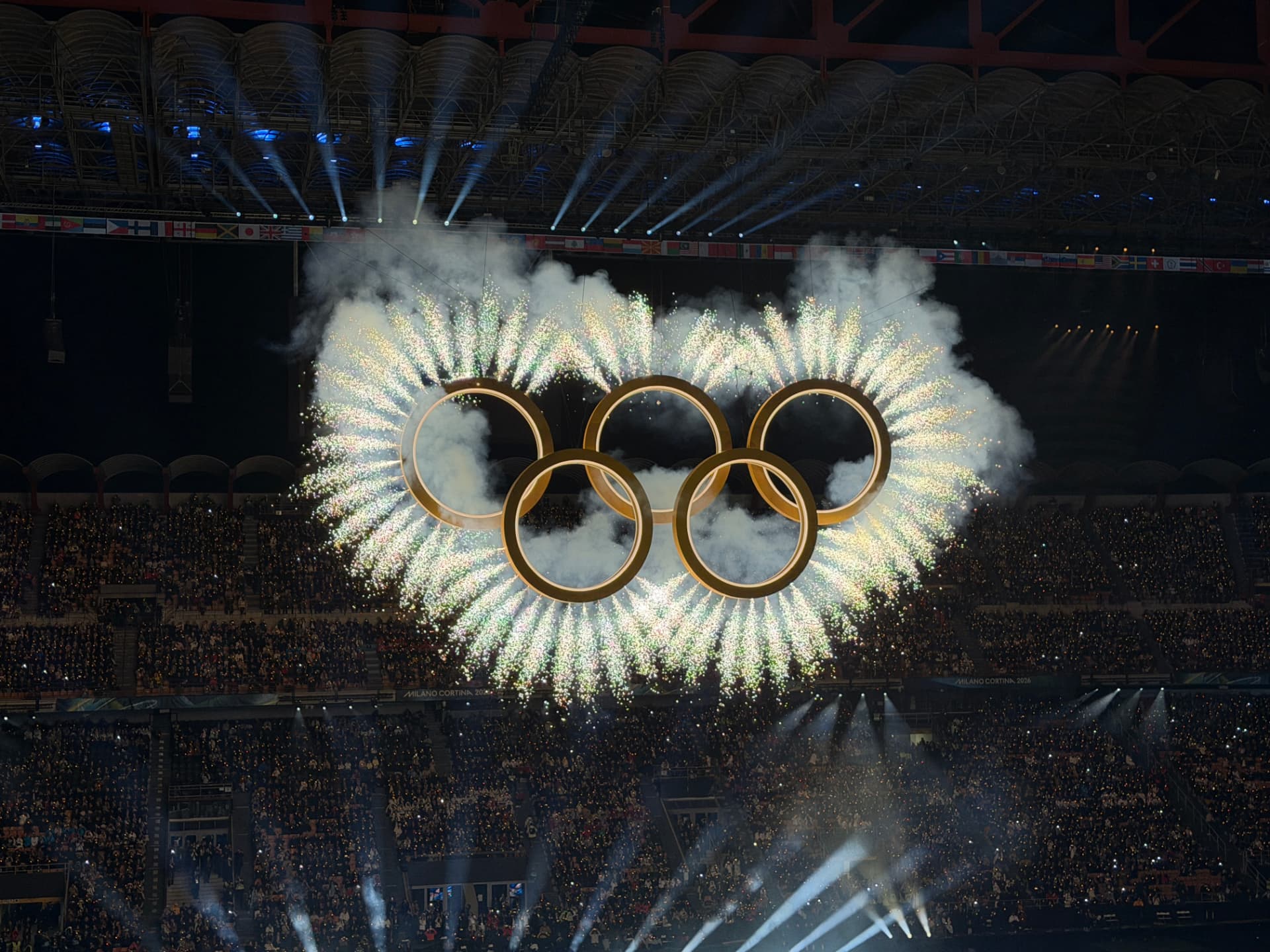 Milano Cortina 2026 — glowing Olympic rings over stadium fireworks